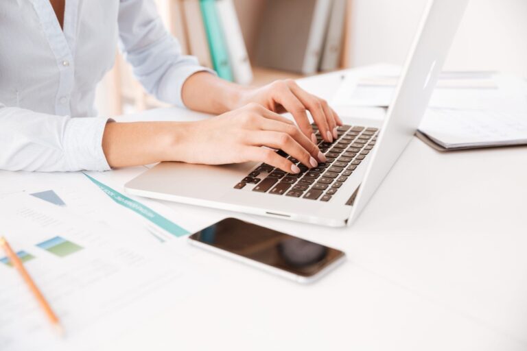 Cropped picture of businesswoman dressed in white shirt sitting in her office and using laptop.